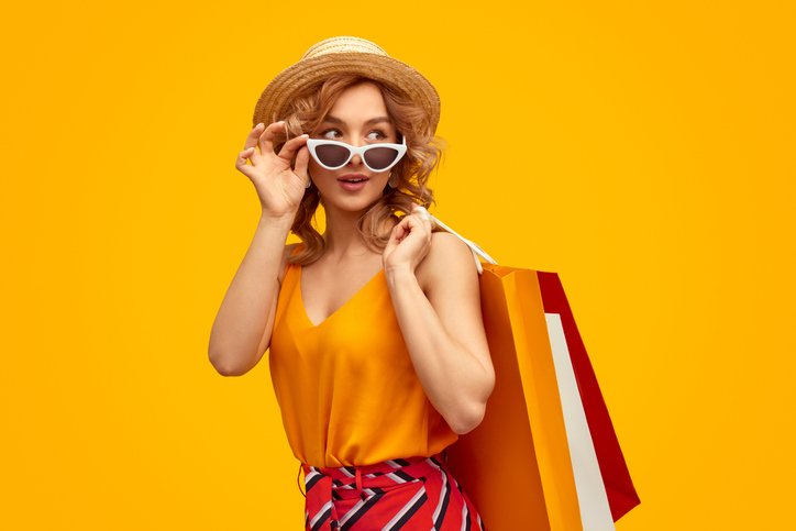 Shopper in a sun hat and sunglasses carrying colorful shopping bags