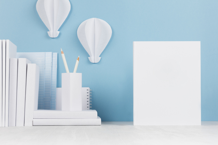 Blank white display board beside books and paper decorations against a blue wall