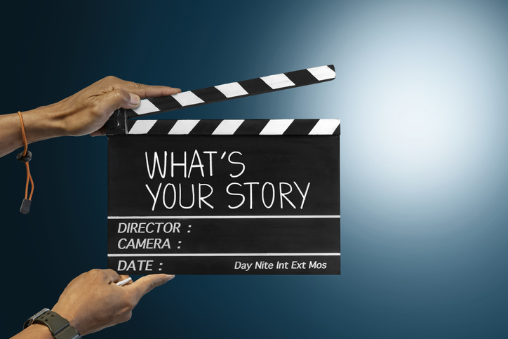 Hands holding a film clapperboard reading “What’s Your Story”